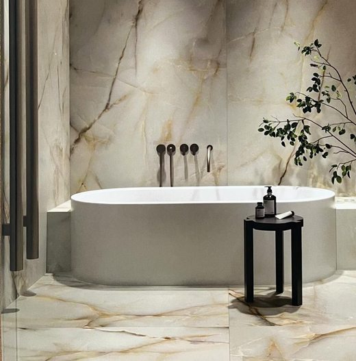 Un bagno moderno caratterizzato da una vasca ovale freestanding bianca addossata a una parete rivestita di piastrelle di marmo venato di tonalità chiara.