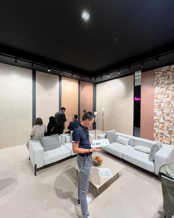 In uno showroom con pareti e divani dai colori chiari, alcune persone si sono riunite attorno a un tavolo centrale per visionare dei campioni di prodotto.