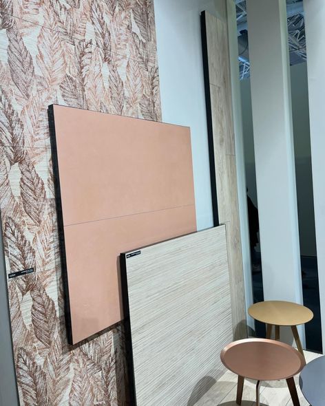 Una composizione che mostra una parete decorata con motivi a foglie, un quadrato color pesca, un pannello effetto legno e due piccoli tavolini rotondi.