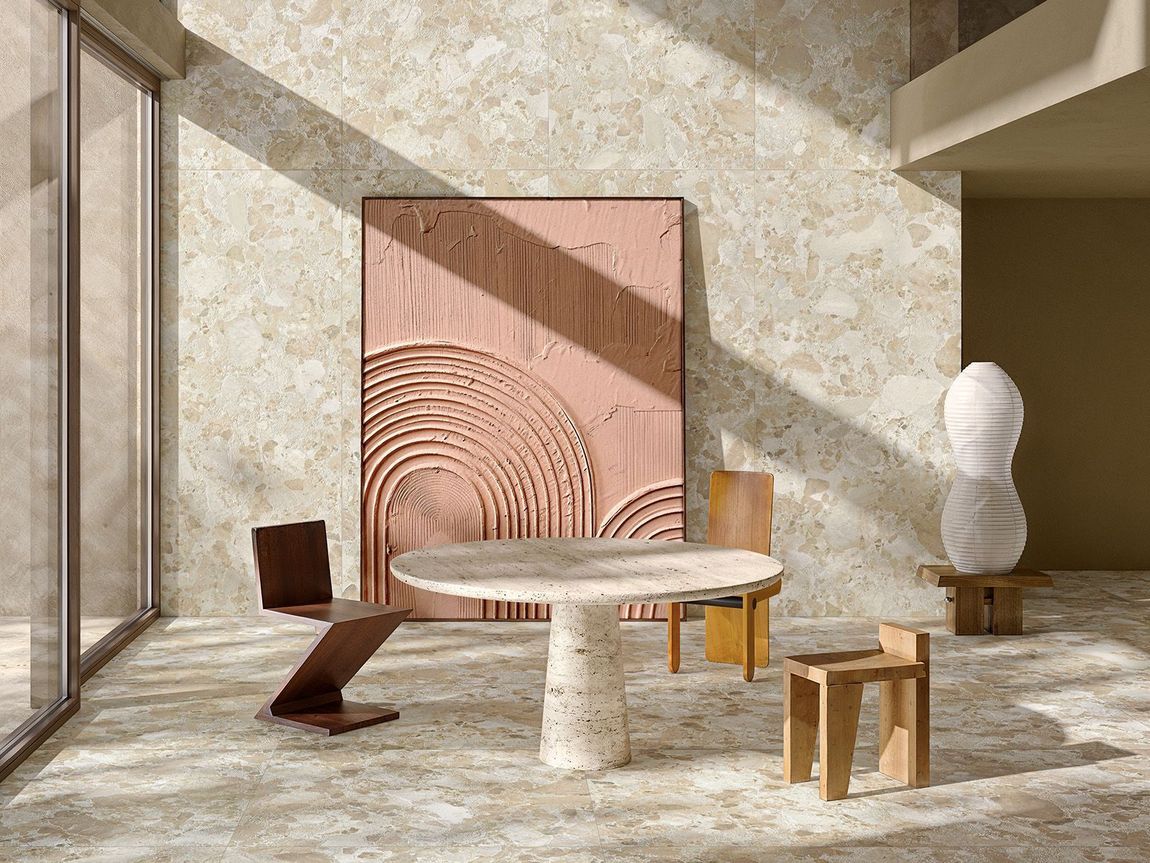 Una stanza moderna e luminosa con un tavolo rotondo in pietra, una sedia a zig-zag, uno sgabello e un'opera d'arte rosa con texture su una parete in pietra.