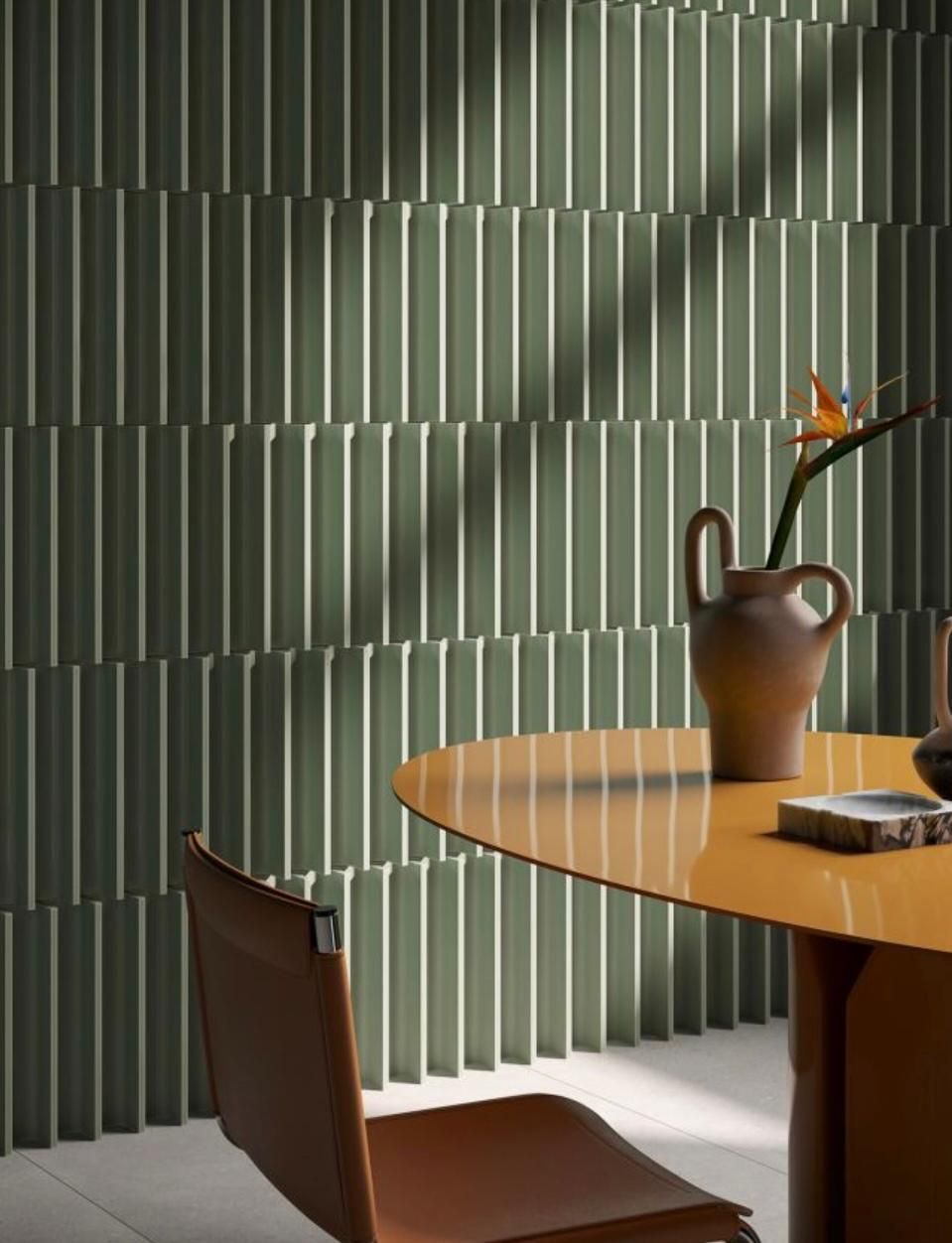 Una zona pranzo caratterizzata da una parete a coste color verde salvia, un tavolo ovale color ambra con un vaso in ceramica e una sedia in pelle marrone.