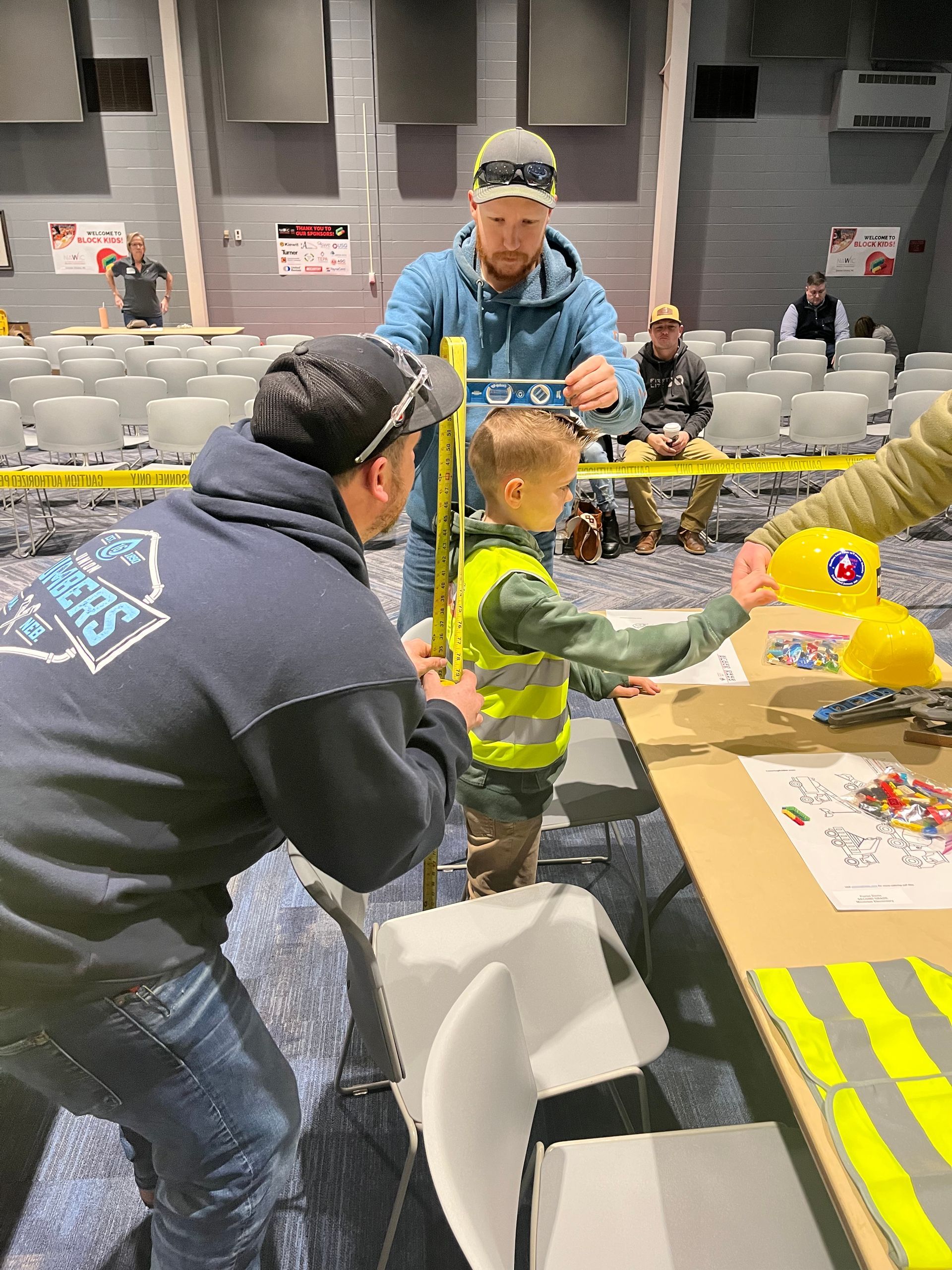 A group of men are standing around a table with a little boy in a yellow vest.