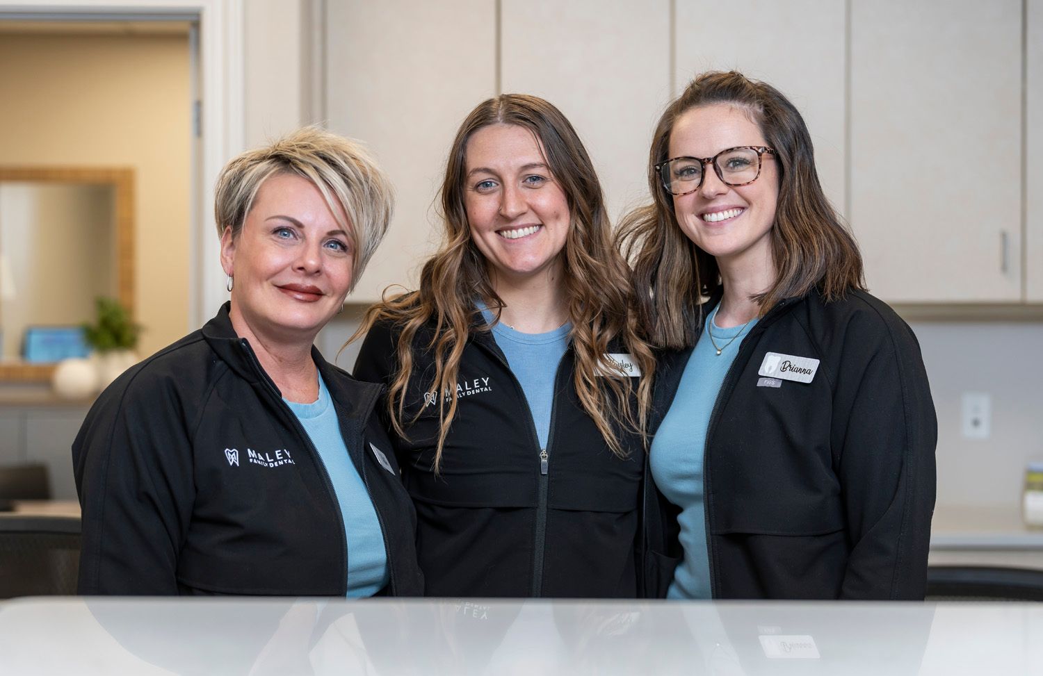 Three staff members are posing for a picture at a desk at Maley Family Dental