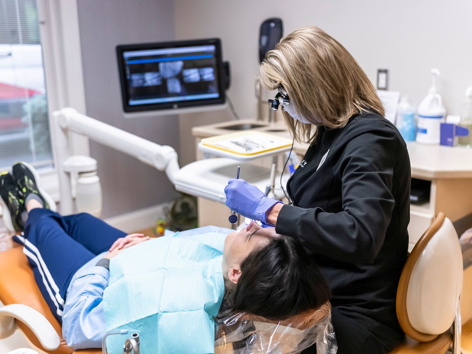 A dental hygienist is examining a woman's teeth in a dental chair at Maley Family Dental