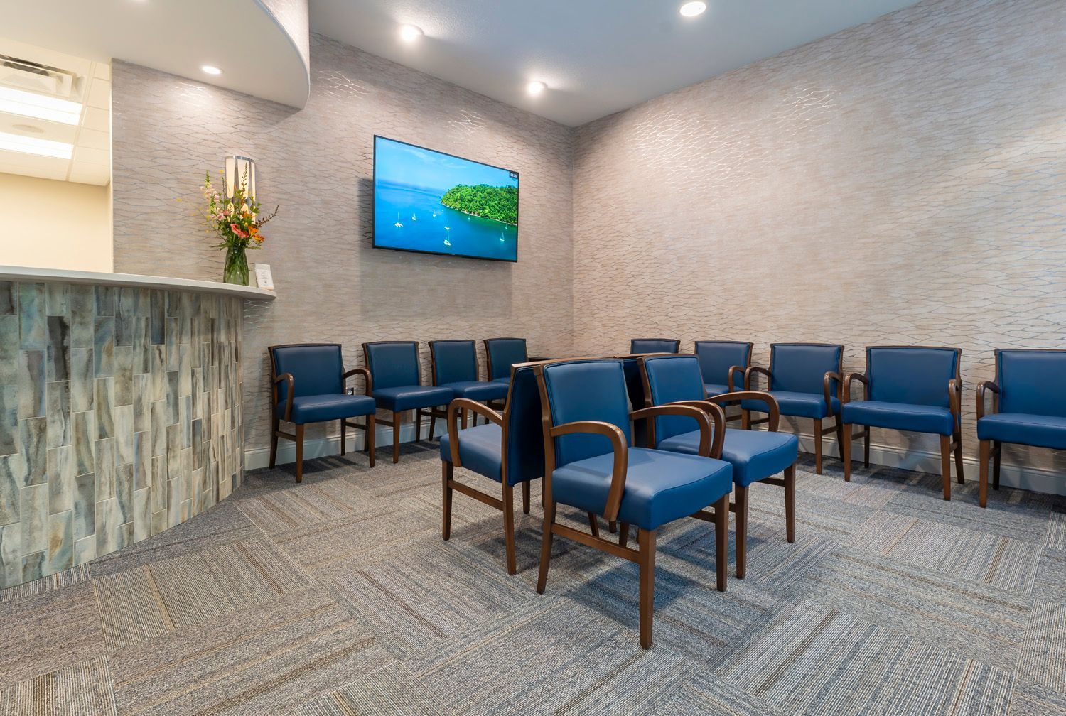 A waiting room with blue chairs and a television on the wall at Maley Family Dental