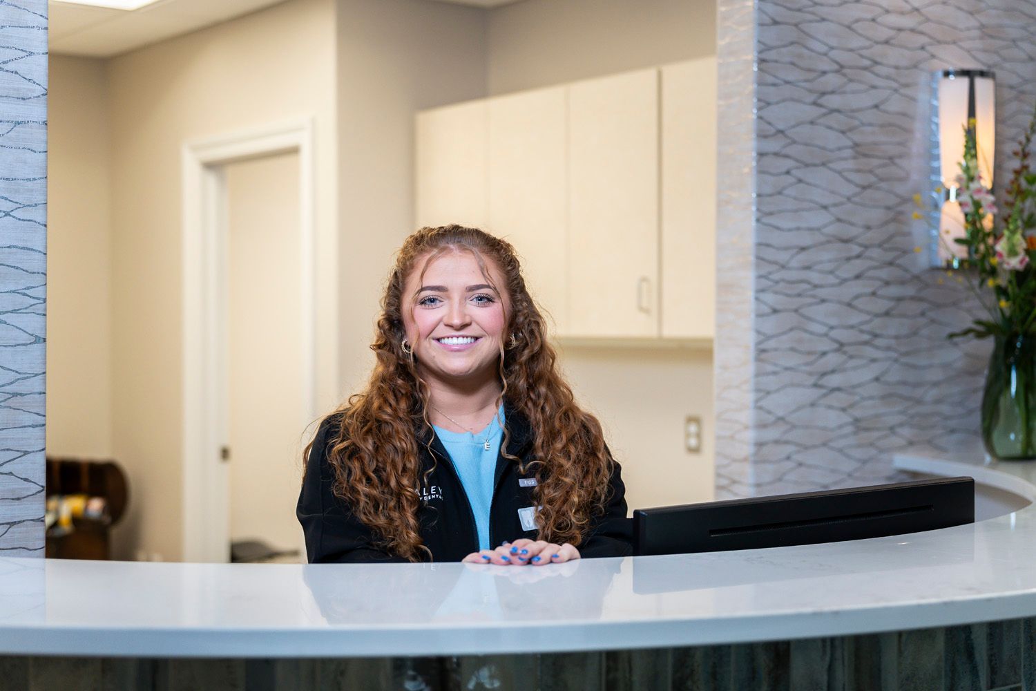 A woman is sitting at a reception desk in a dental office at Maley Family Dental