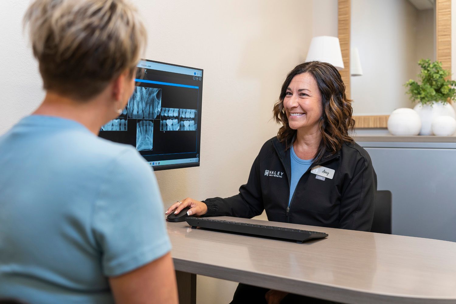 A dental hygienist is sitting at a desk showing a patient her teeth x-rays at Maley Family Dental