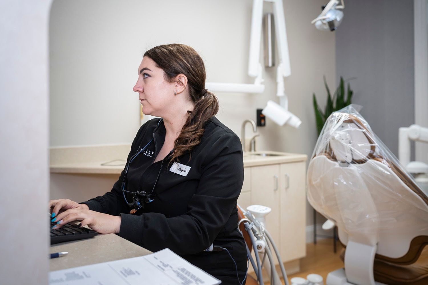 A hygienist is sitting at a desk in a dental office using a computer at Maley Family Dental