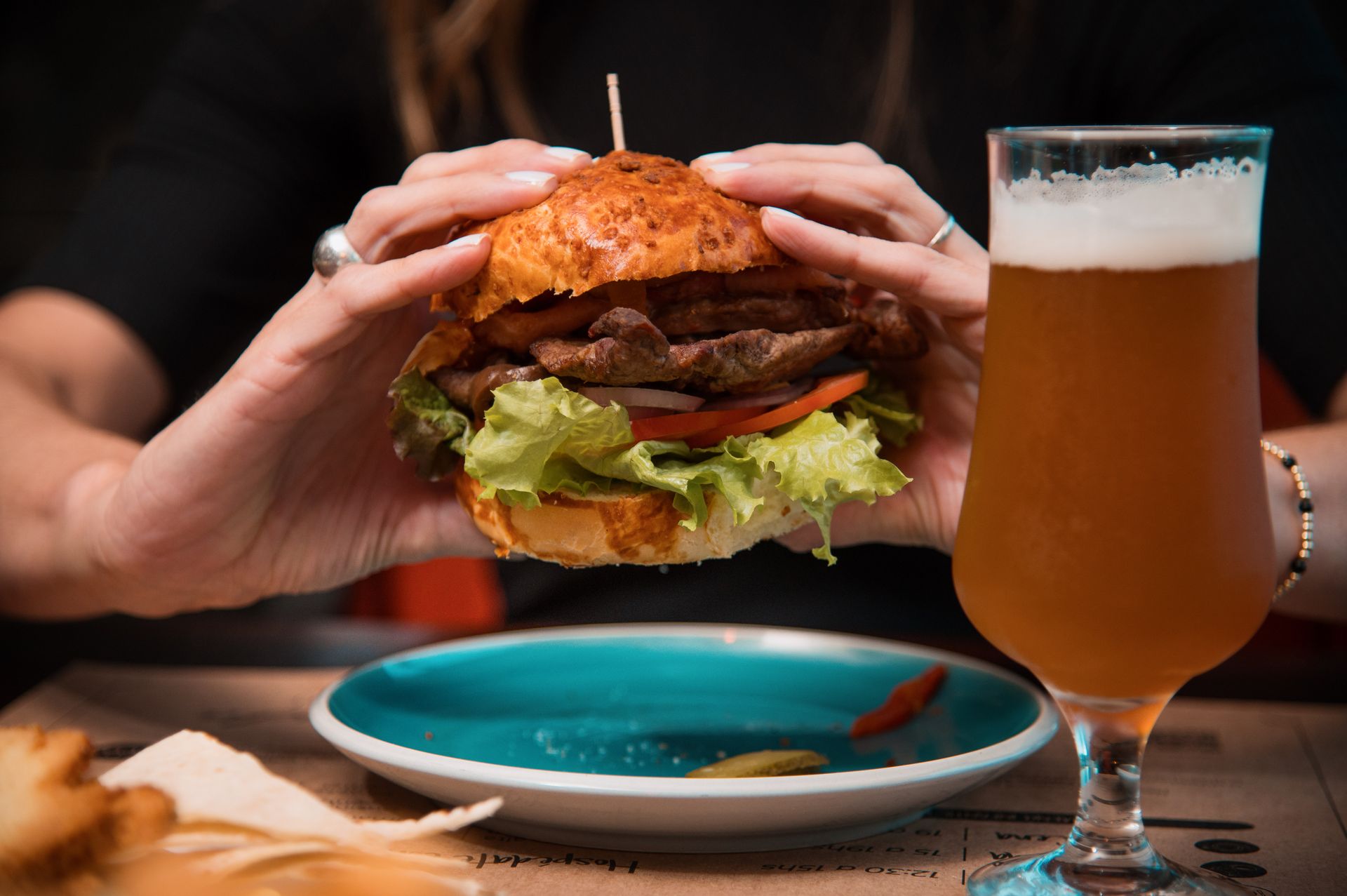 Una persona sostiene una hamburguesa junto a un vaso de cerveza.