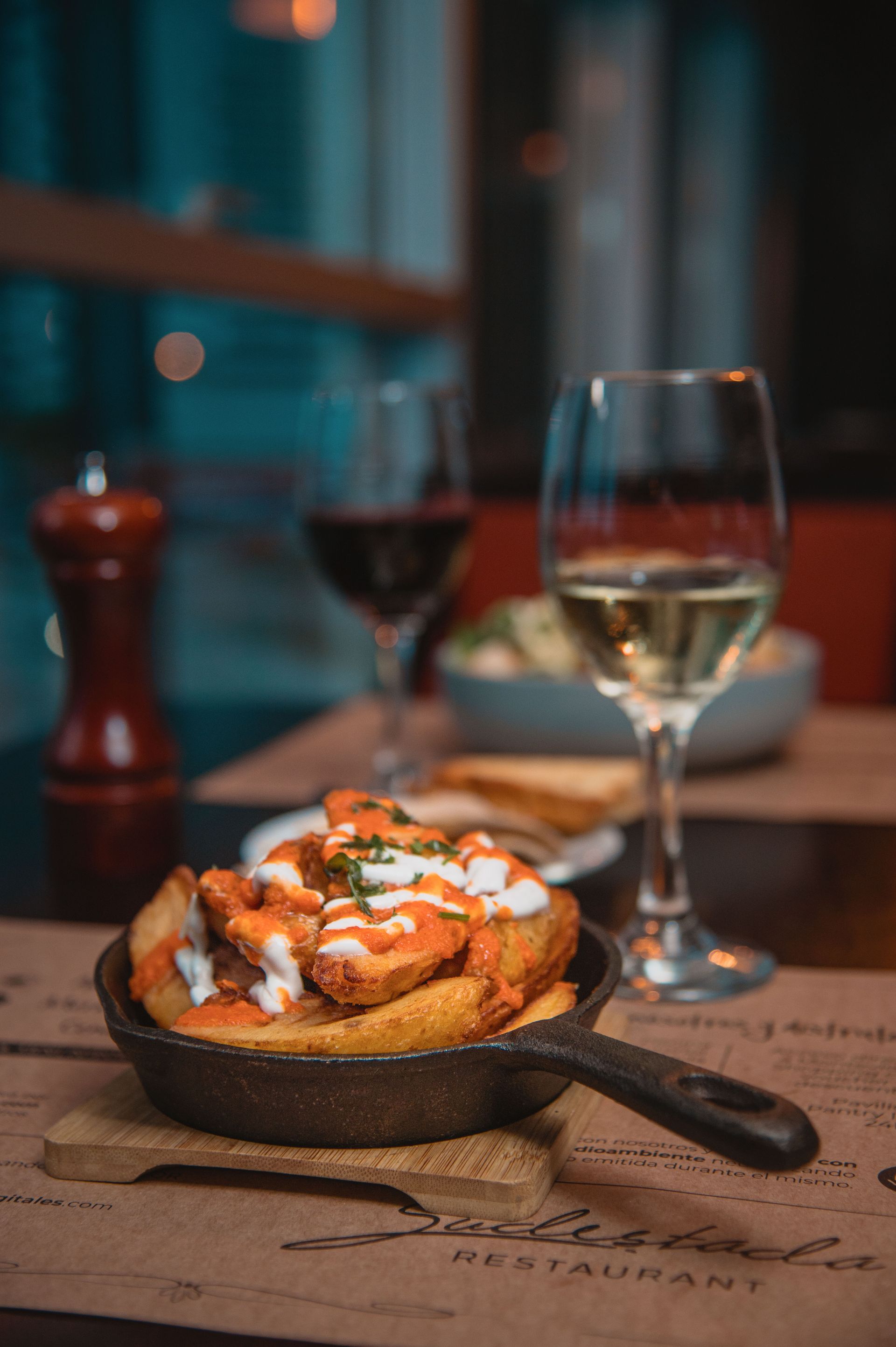 Una cacerola con comida está sobre una mesa junto a una copa de vino.