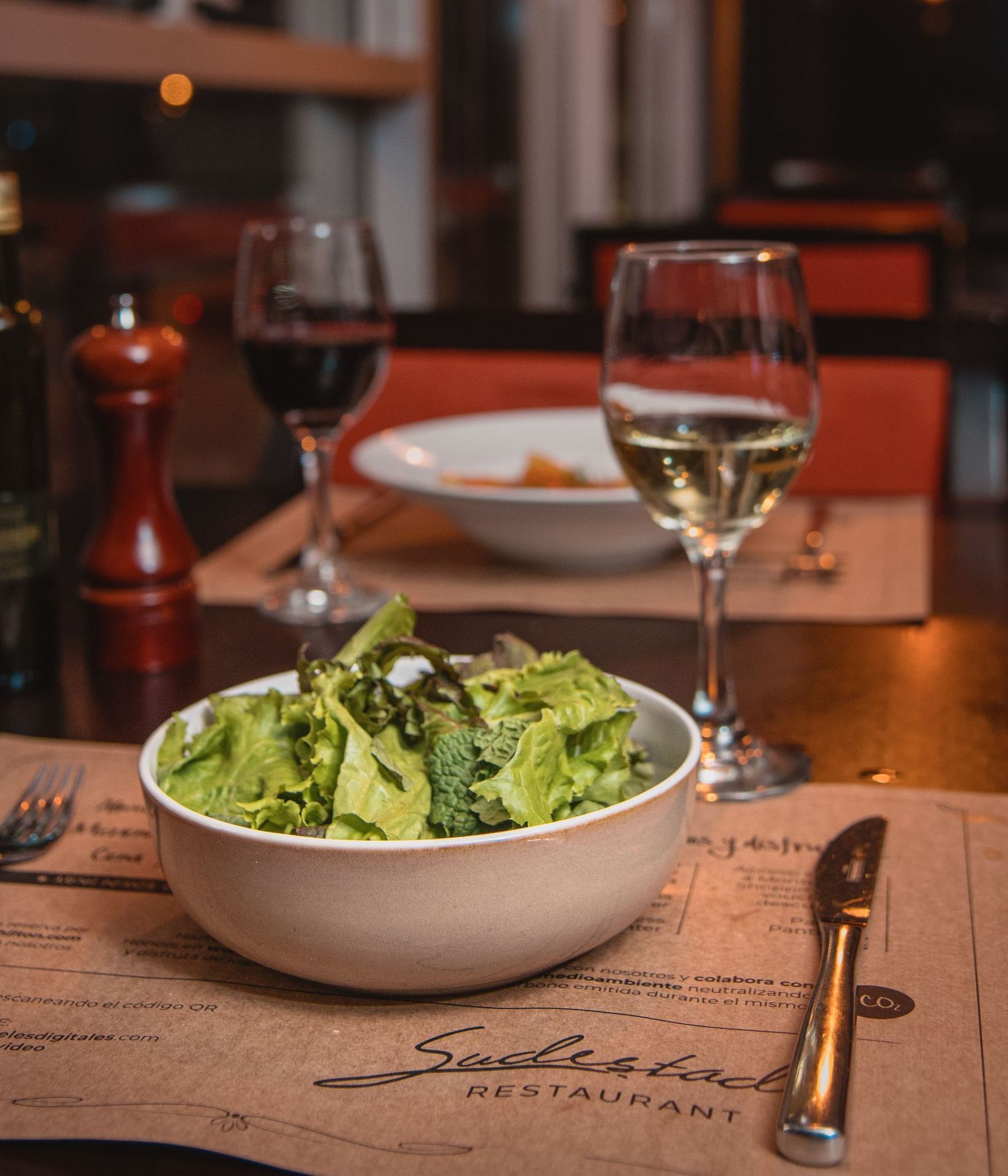 Un plato de ensalada se encuentra en una mesa junto a copas de vino.