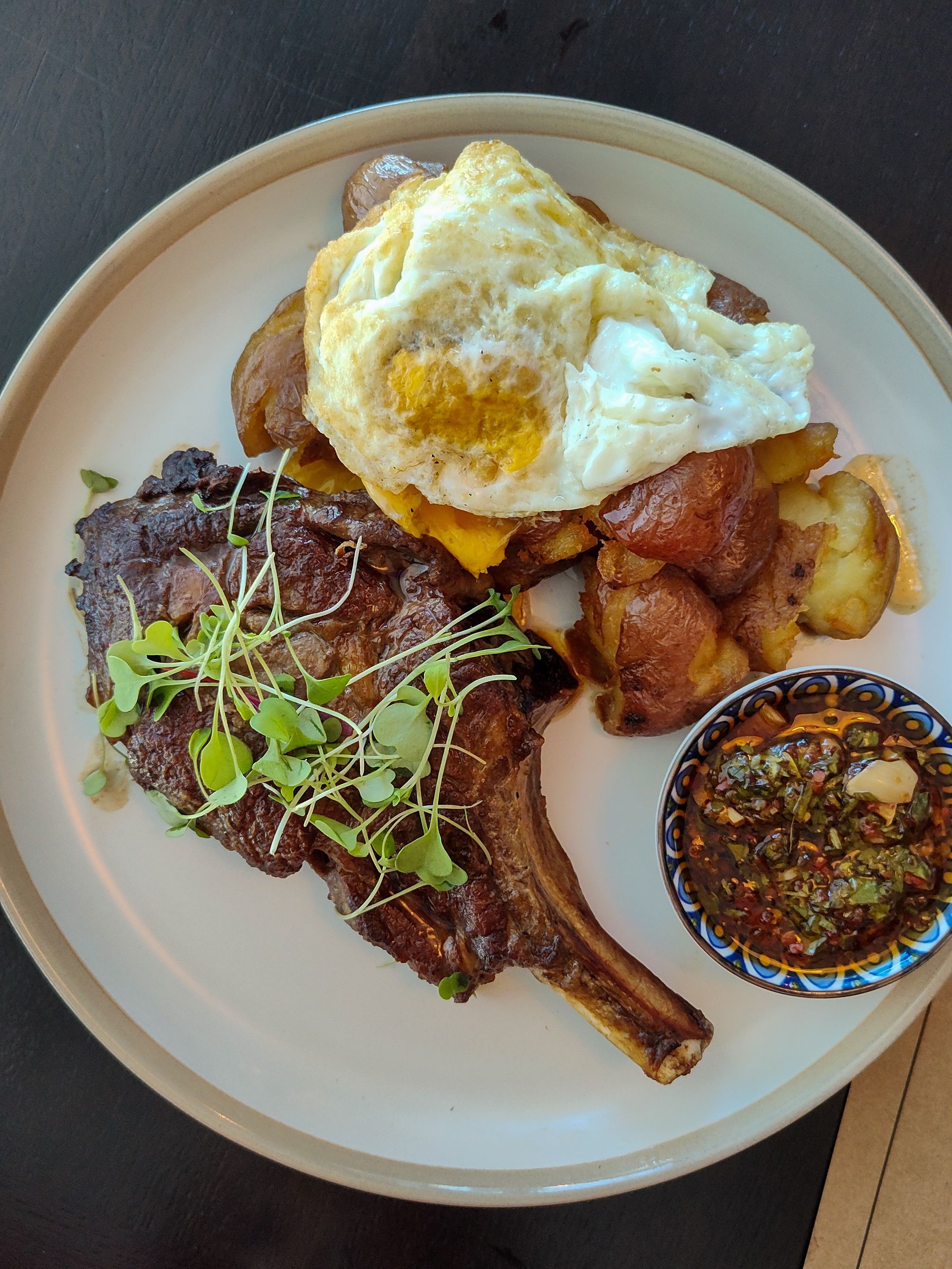 Un plato blanco cubierto con bistec, huevos, patatas y salsa.