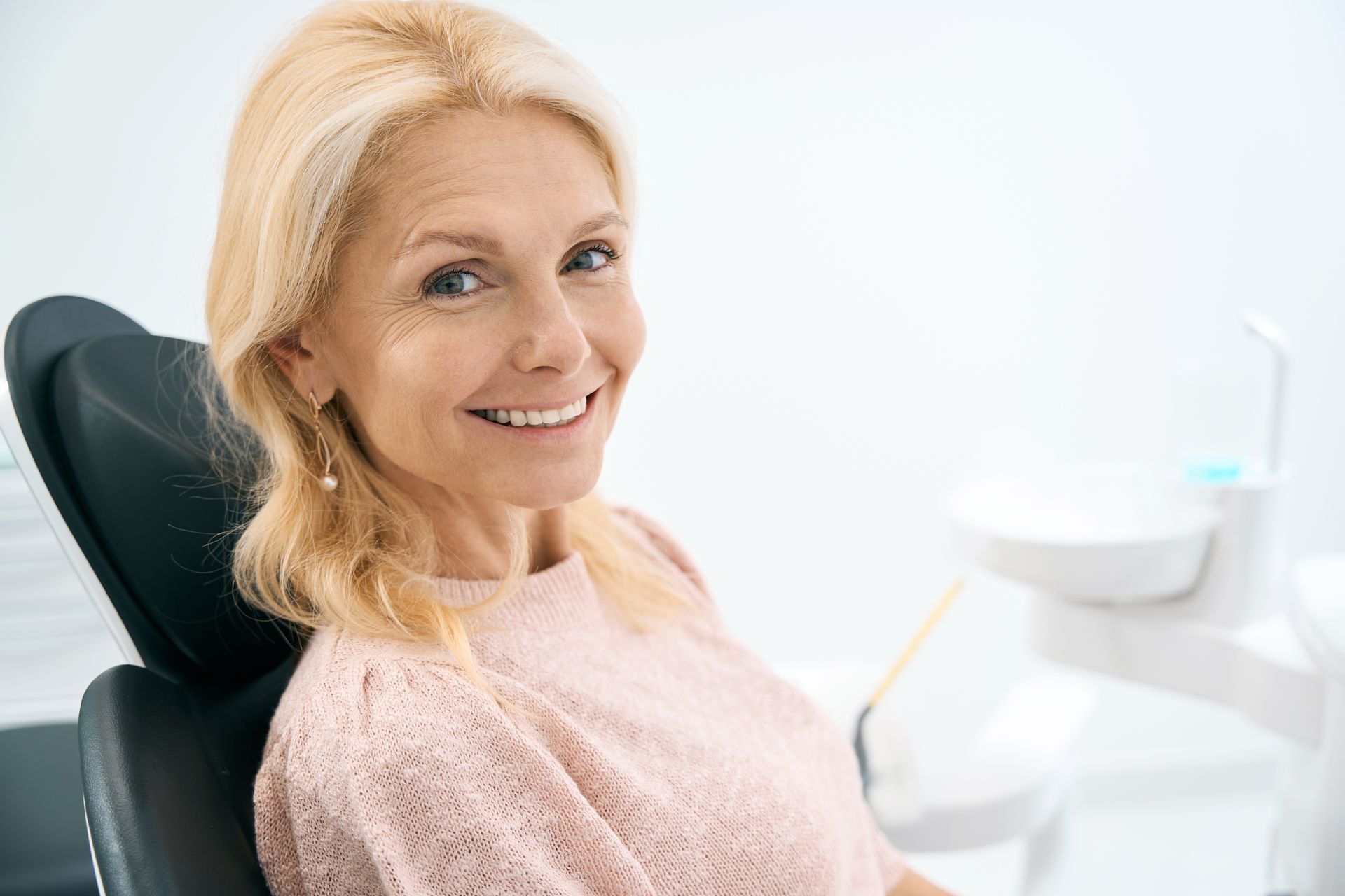 Patient seated in a dental chair showing teeth during an exam in a bright clinic.