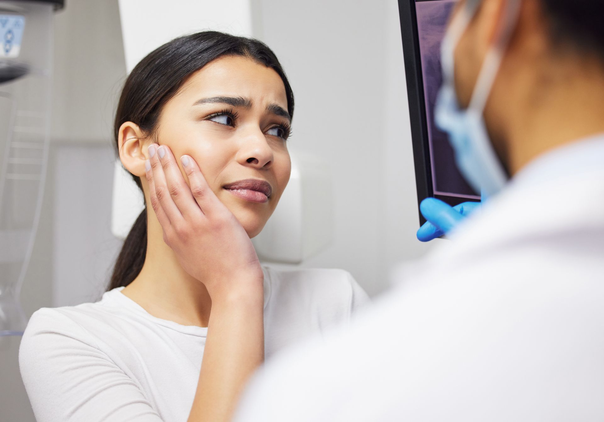 Patient holding her jaw in pain while consulting with professional emergency dentists.