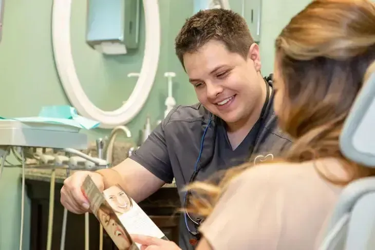 Dentist smiling, showing patient a brochure in a dental office.