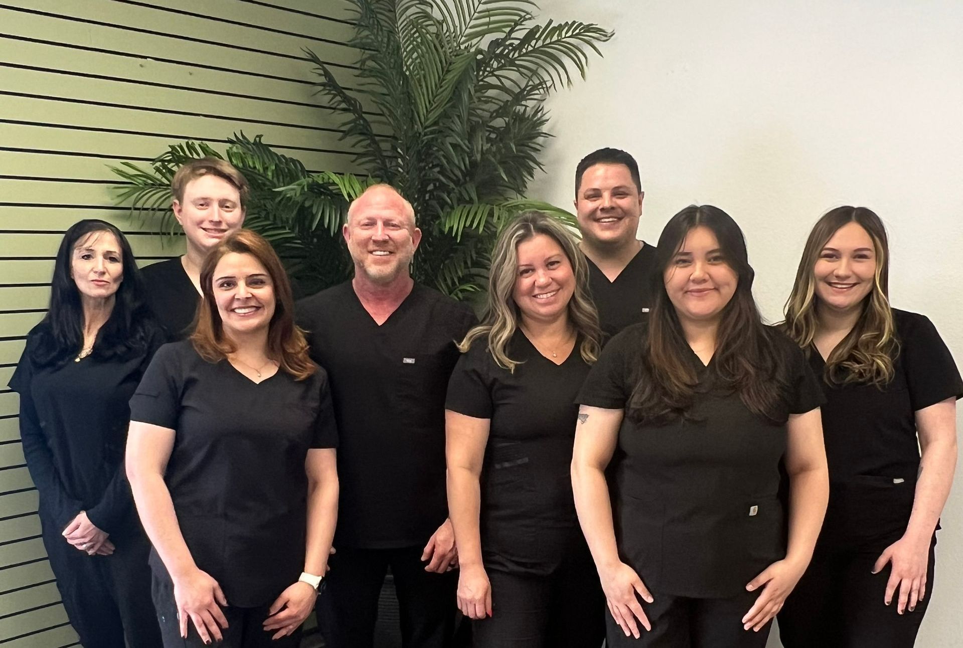 Group of eight people in black scrubs posing for a photo in a clinic setting.