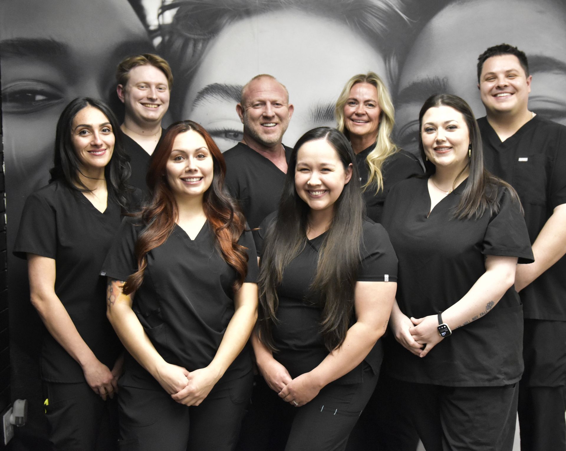 Group of eight people in black scrubs posing for a photo in a clinic setting.