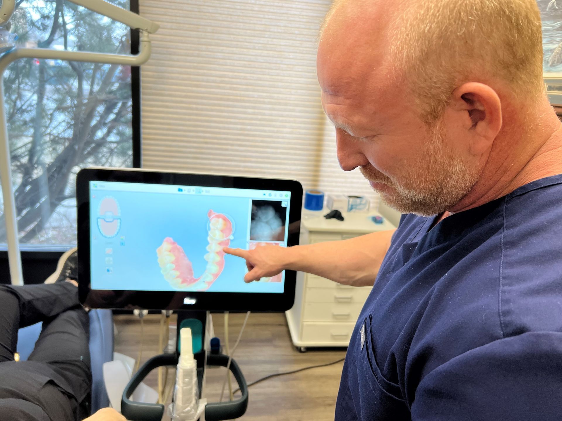 Dentist pointing at a 3D model of teeth on a monitor in an office setting.