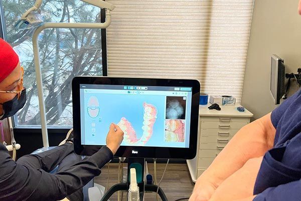 Dentist pointing to teeth scan on a monitor, explaining procedure to patient in office.