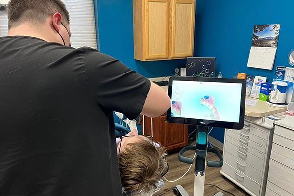 Dentist treating patient's teeth, with a screen showing an image of the patient's teeth, in a dental office.