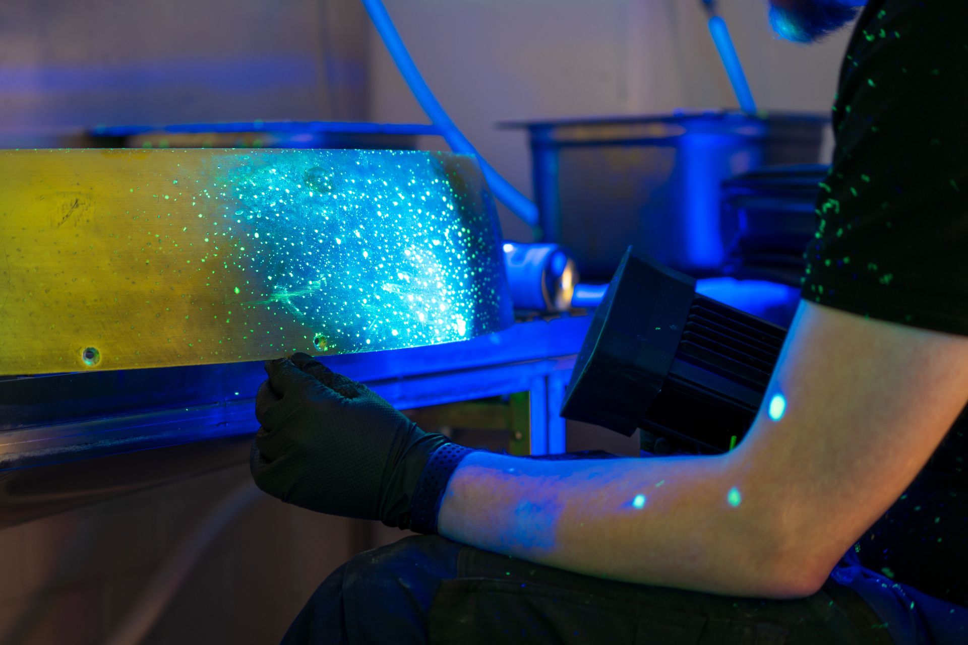 Person in black gloves examines glowing cylinder under blue light in a lab.