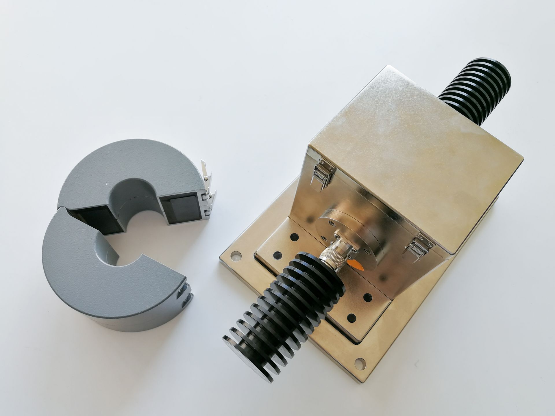 Split gray ferrite core next to a metal device with coaxial connectors and black heat sinks, on a white surface.