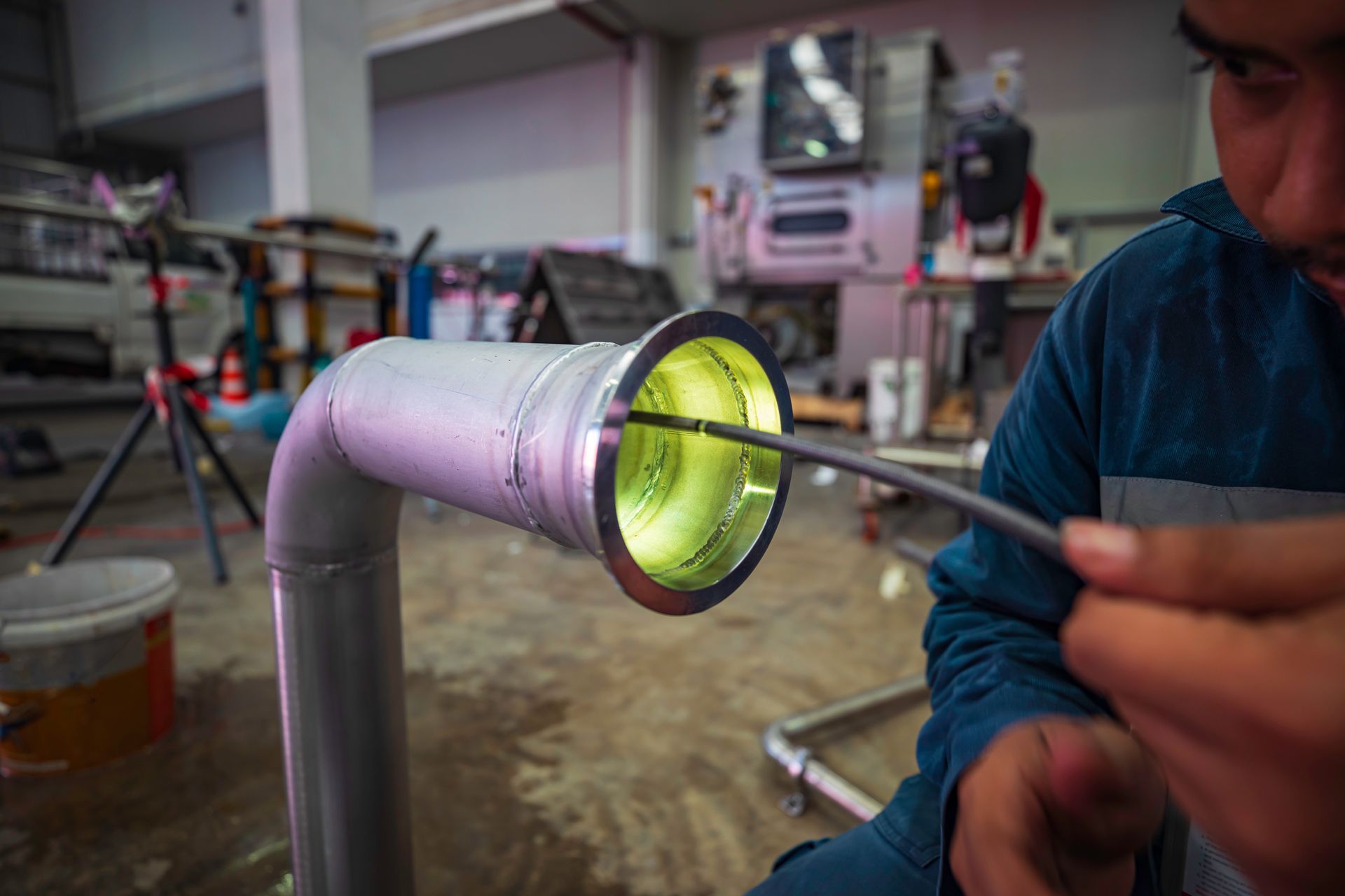 Technician using a tool to inspect a glowing yellow pipe in a workshop