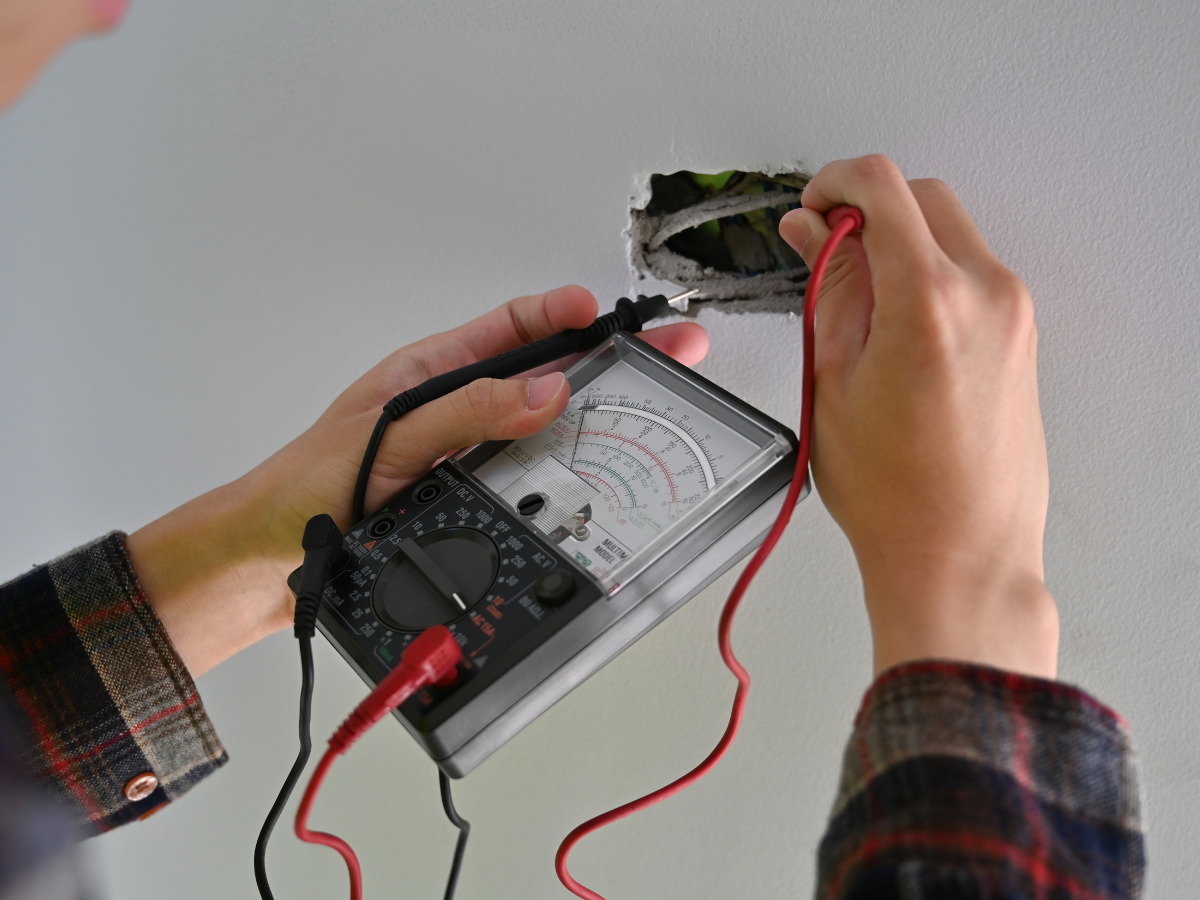 Person using a multimeter to test an electrical outlet, holding probes in its slots. Person using a multimeter to test an electrical outlet, holding probes in its slots.