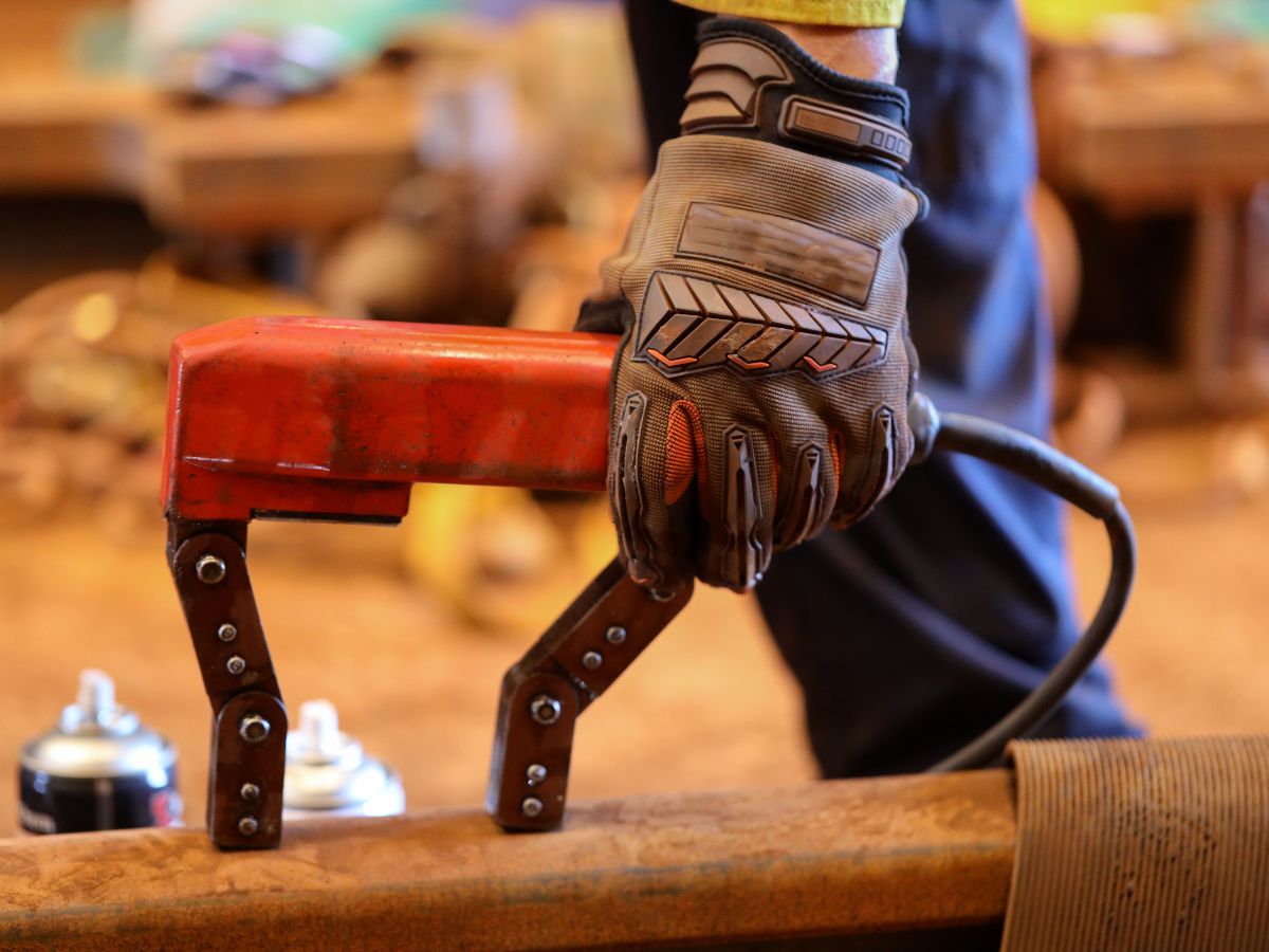 Gloved hand holding a red clamp, attached to metal beam. Work setting.