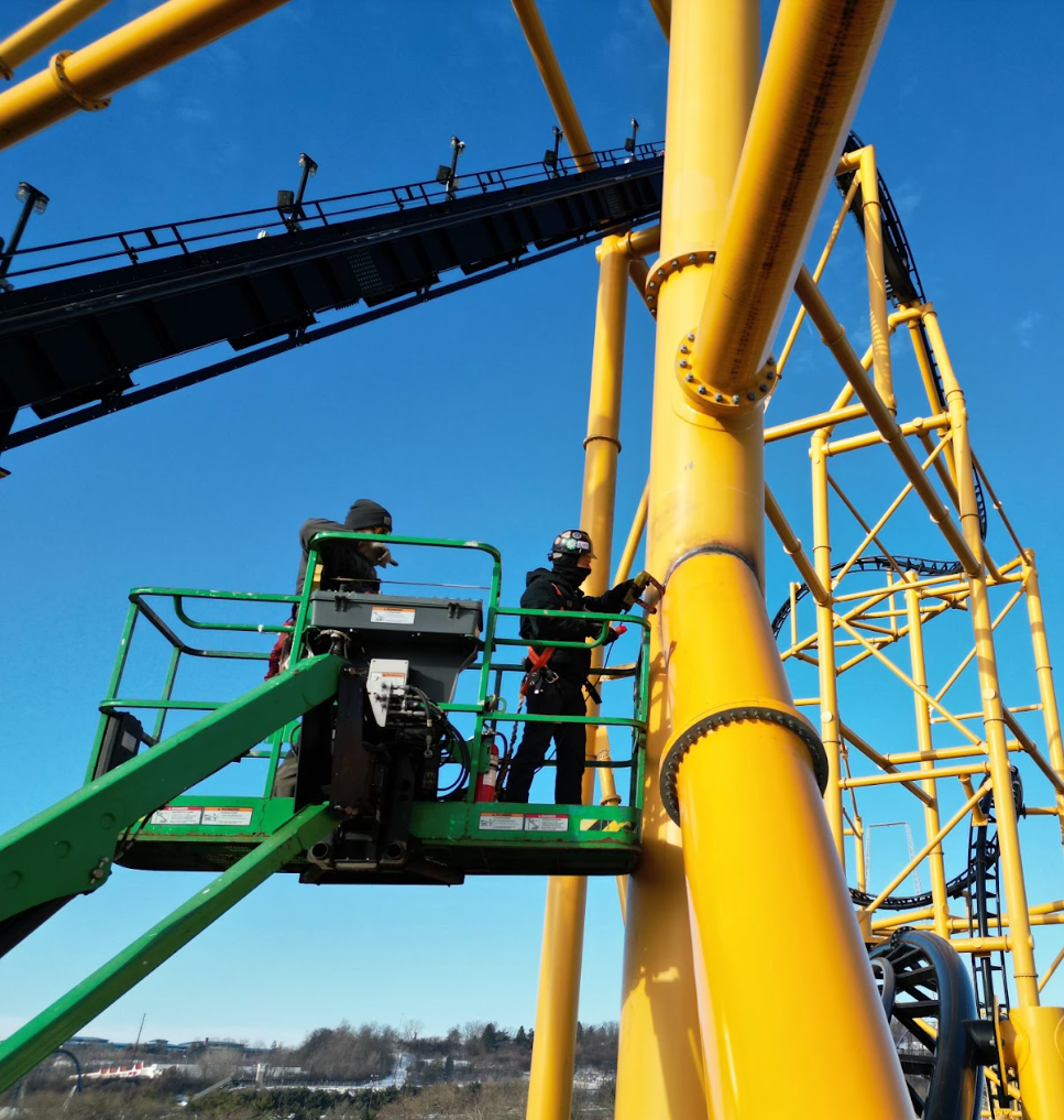 A man in a green cage is working on a yellow structure