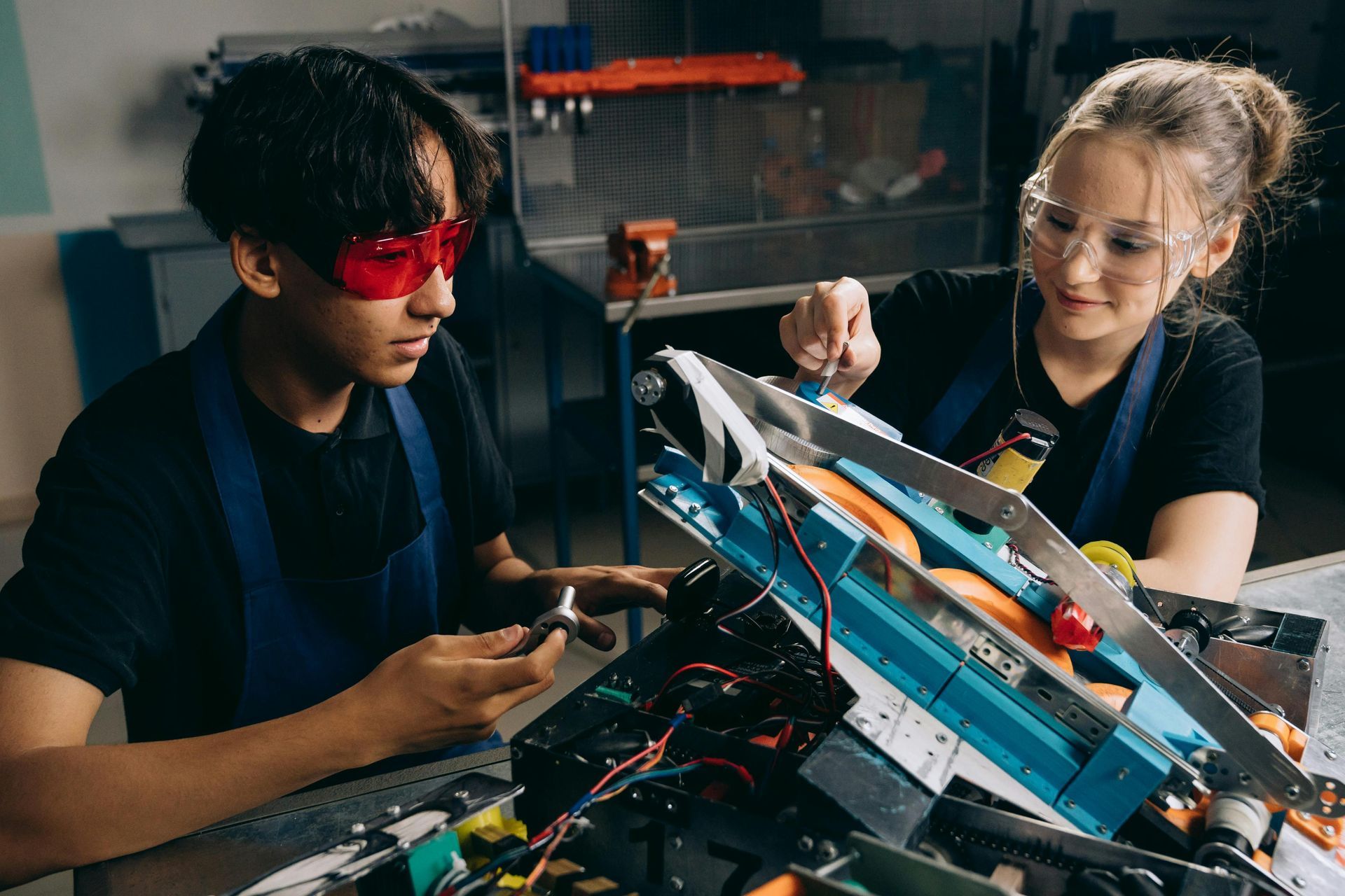 A man and a woman are working on a robot in a garage.