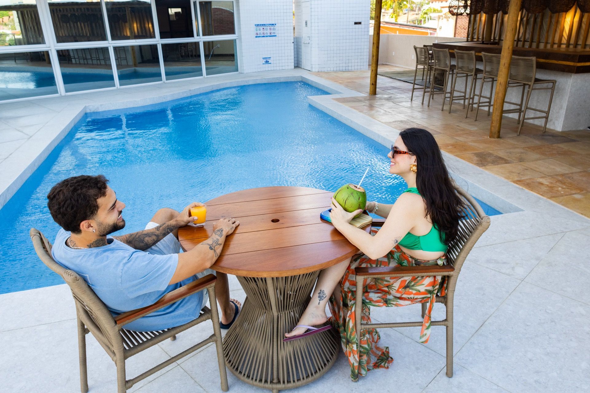 Um homem e uma mulher estão sentados à mesa em frente a uma piscina.