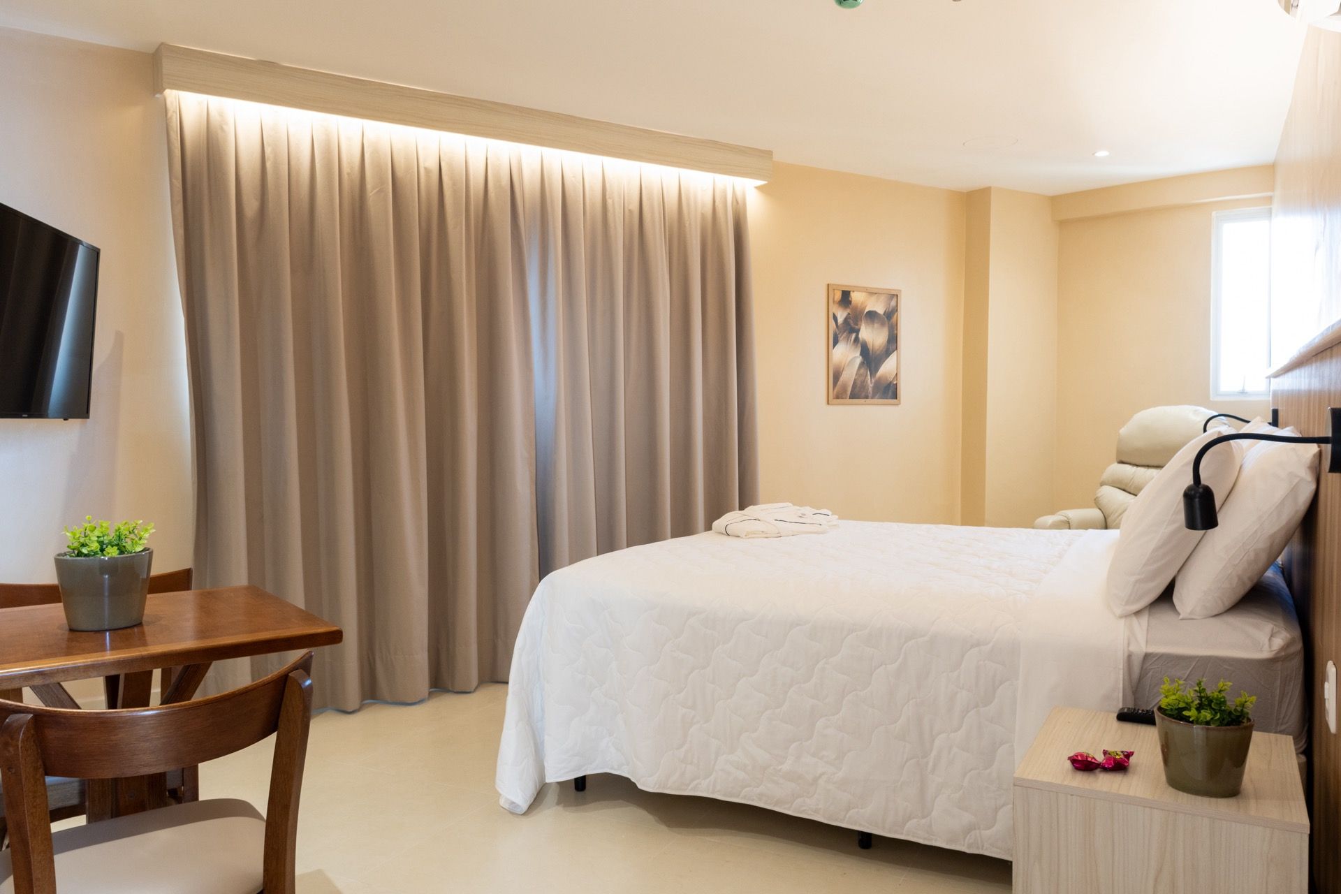 Um quarto de hotel com uma cama, mesa, cadeiras e televisão.