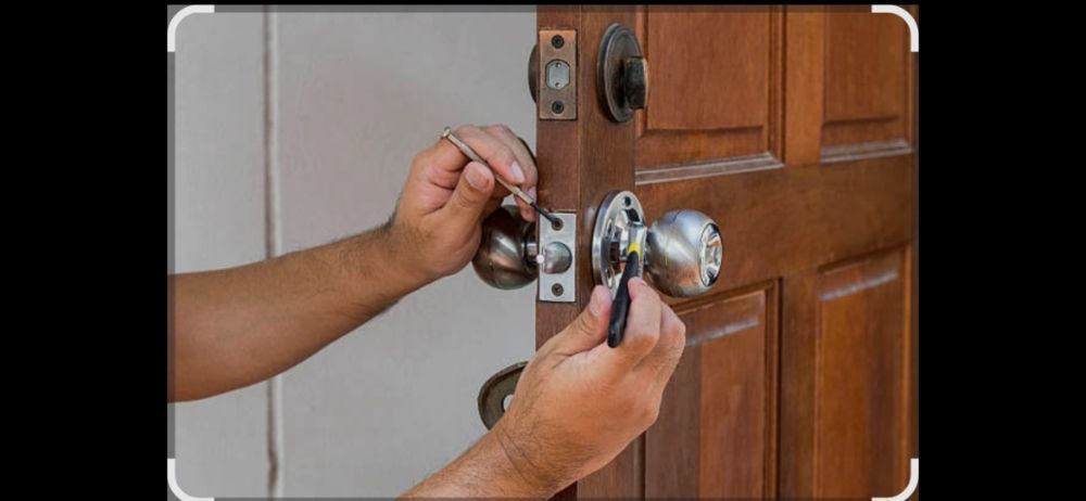 A person's hands using a tool to open a door lock on a brown wooden door.