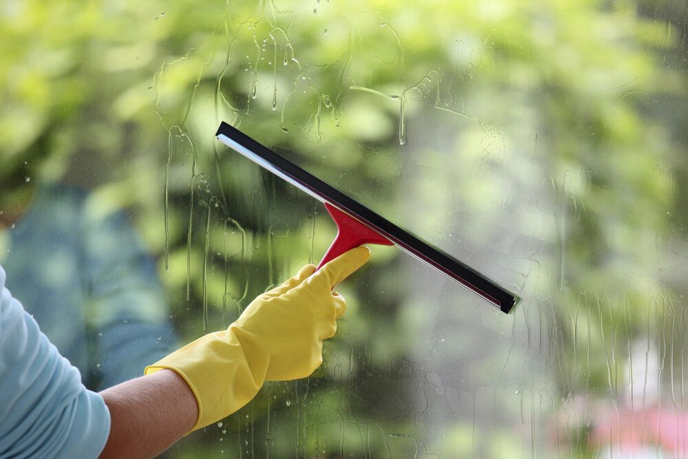 Person Wearing Yellow Gloves is Cleaning a Window With a Squeegee — Abstract Window Cleaning in Tweed Heads, NSW