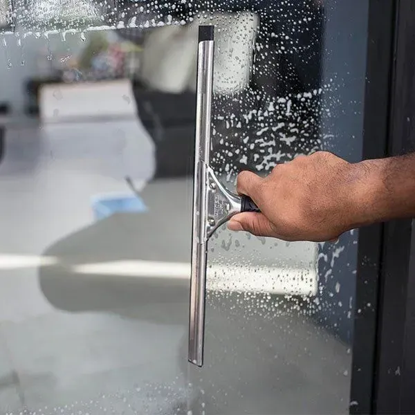 Person is Cleaning a Glass Door With a Squeegee — Abstract Window Cleaning in Hopkins Creek, NSW
