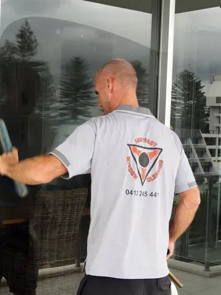 Man Wearing a Grey Shirt With a Triangle on the Back is Cleaning a Window — Abstract Window Cleaning in Hopkins Creek, NSW