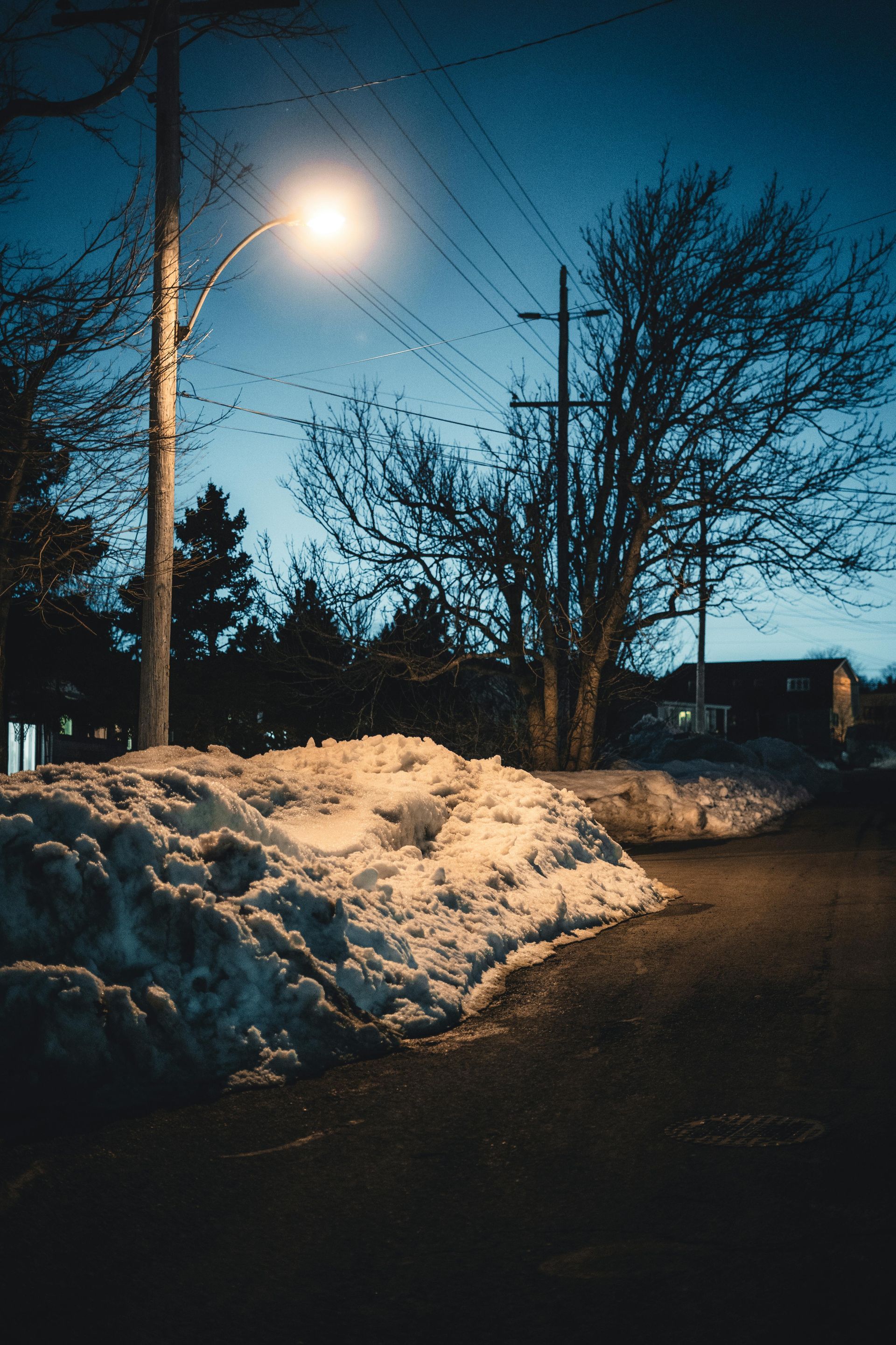 A street light is shining on a snowy sidewalk at night.
