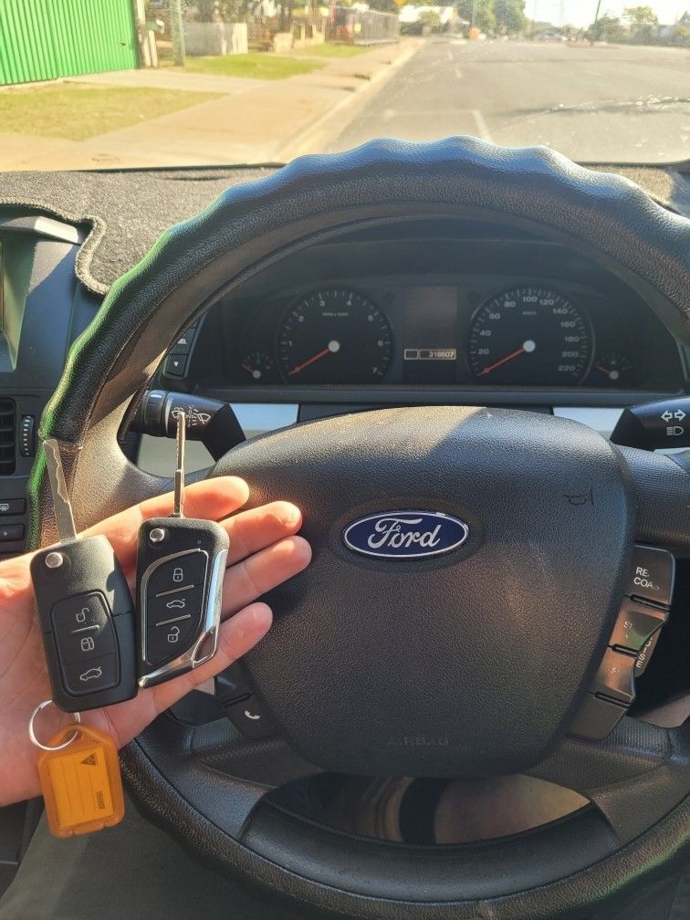 Hand Holding Car Keys in Front of a Ford Steering Wheel — Shaine Hunter Locksmiths in Normanton, QLD