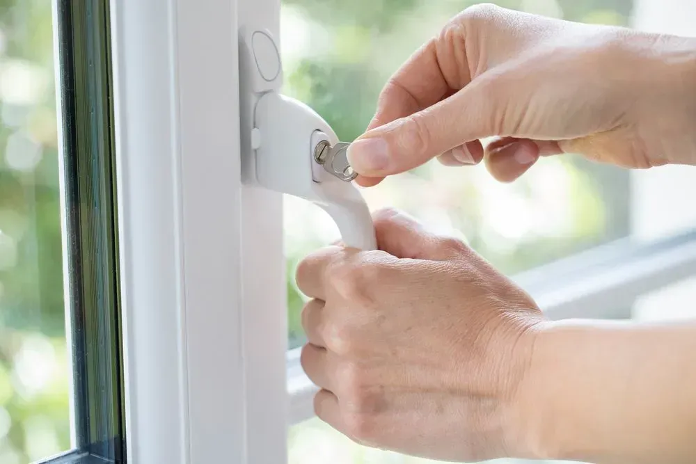 Hands Turning a Key in a White Window Handle, Unlocking the Window — Shaine Hunter Locksmiths in Cloncurry, QLD