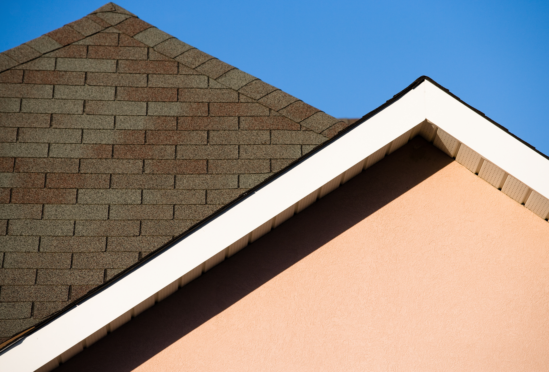 A roof and a side of a house against a blue sky