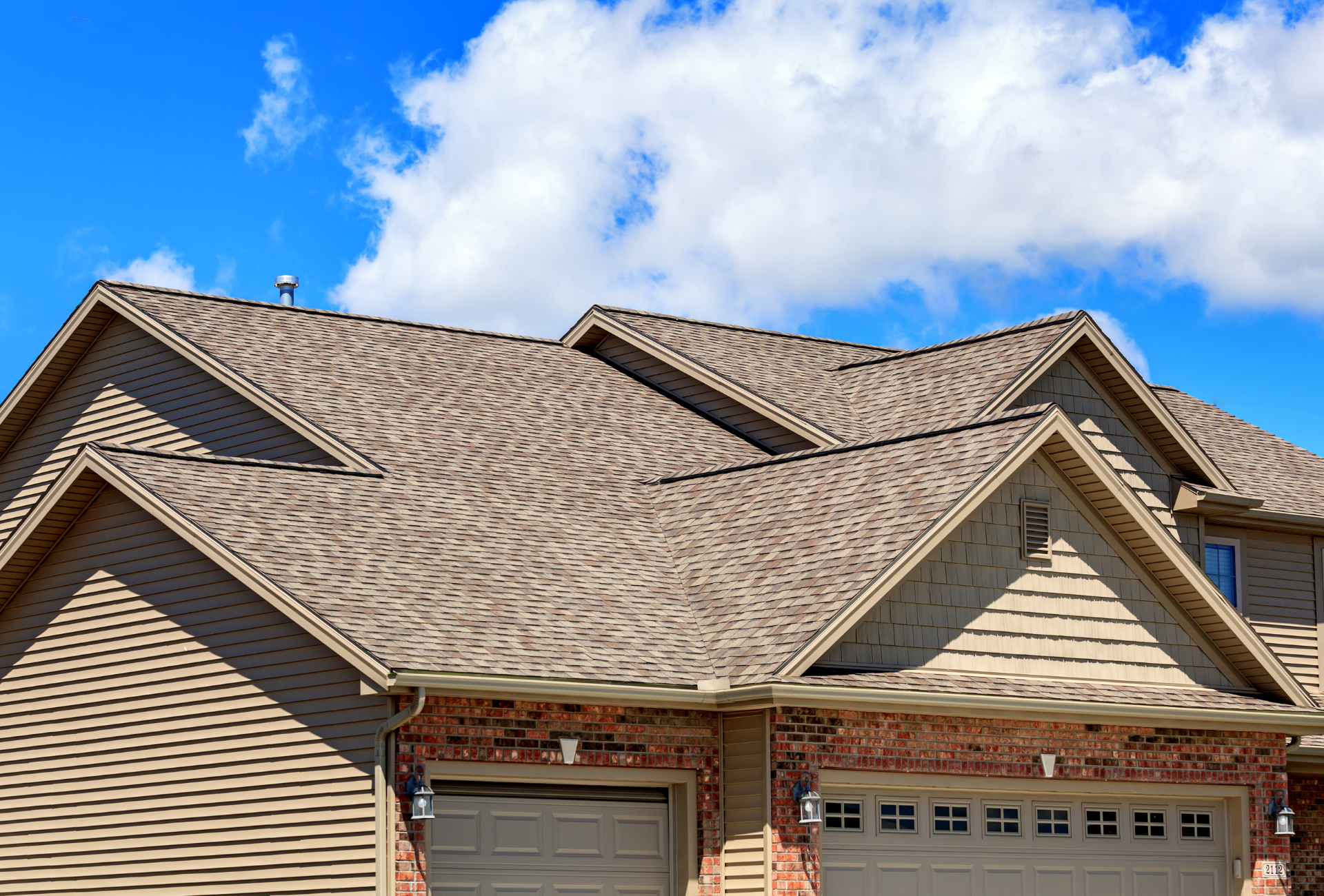The roof of a house with a garage door and a blue sky in the background.
