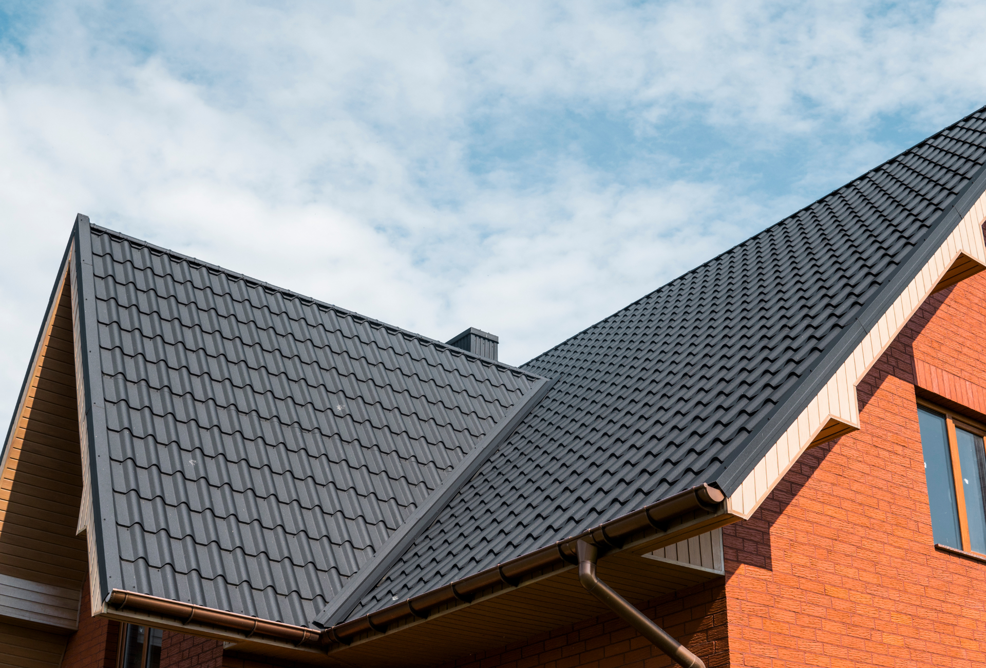 A brick house with a black roof and a blue sky in the background.