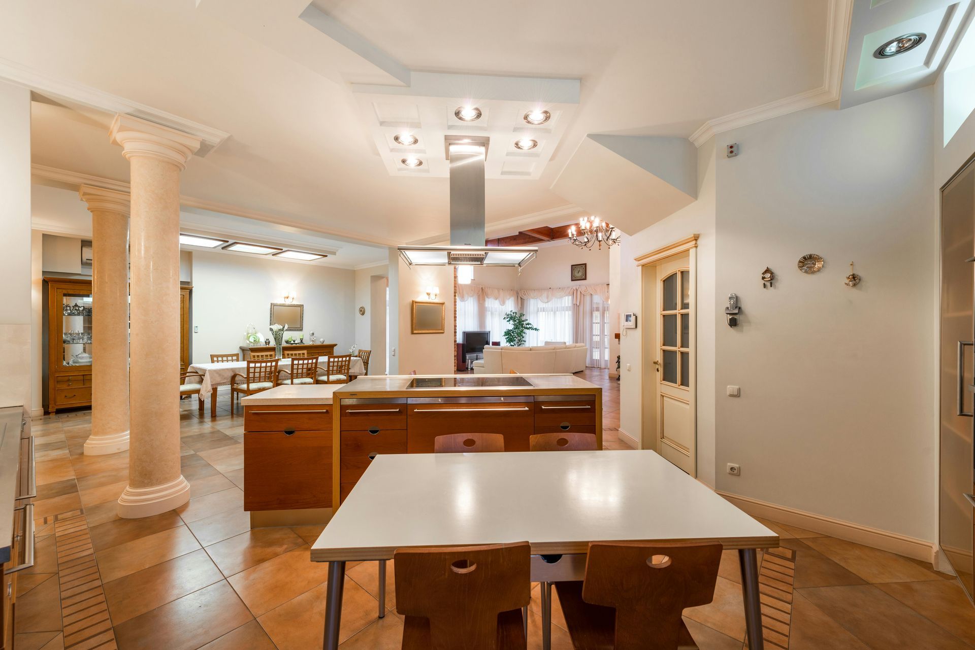 Bright kitchen with wooden cabinets, white table and chairs, pillars, and a dining area in the background.