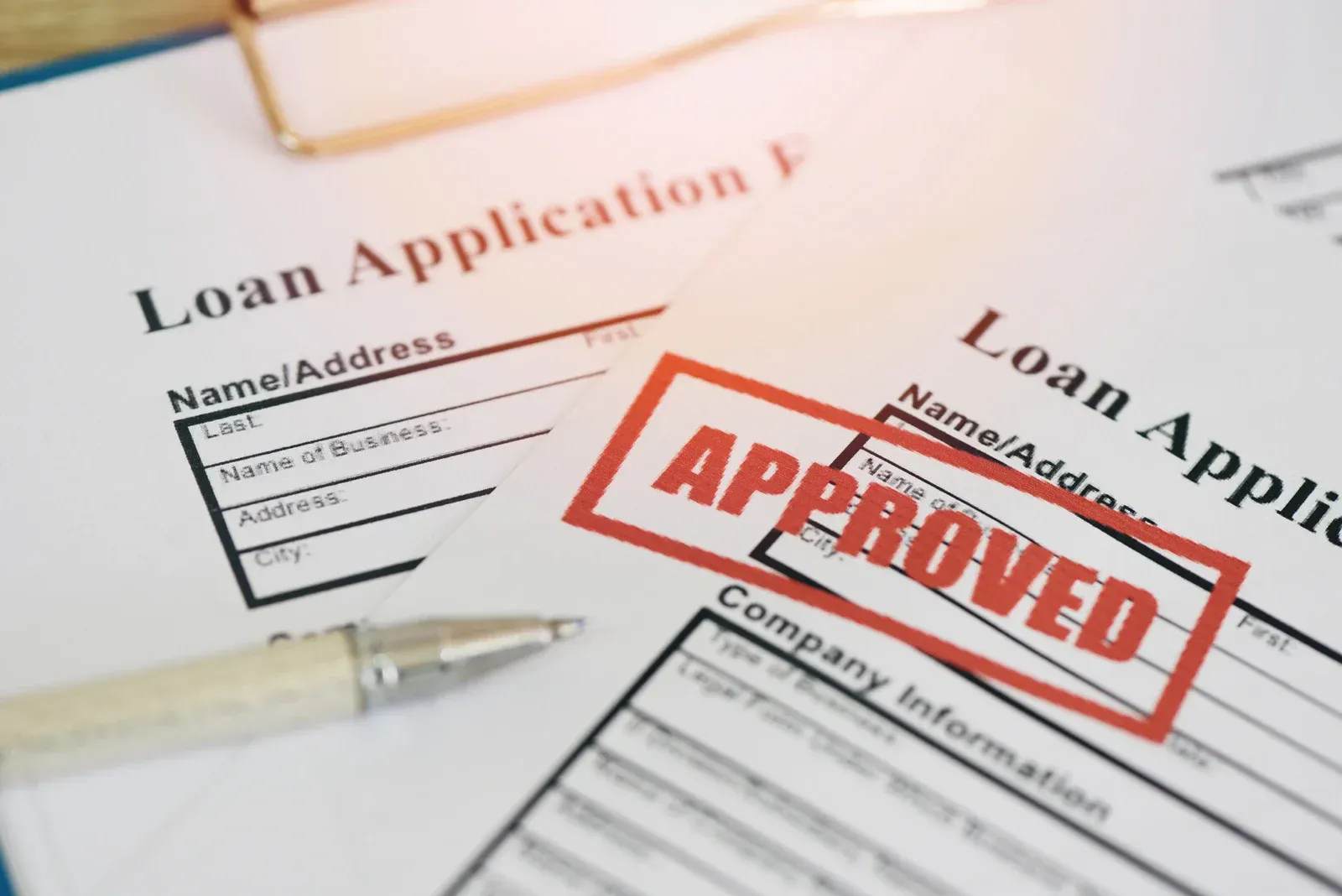 Loan application forms with a red “APPROVED” stamp and pen on a desk