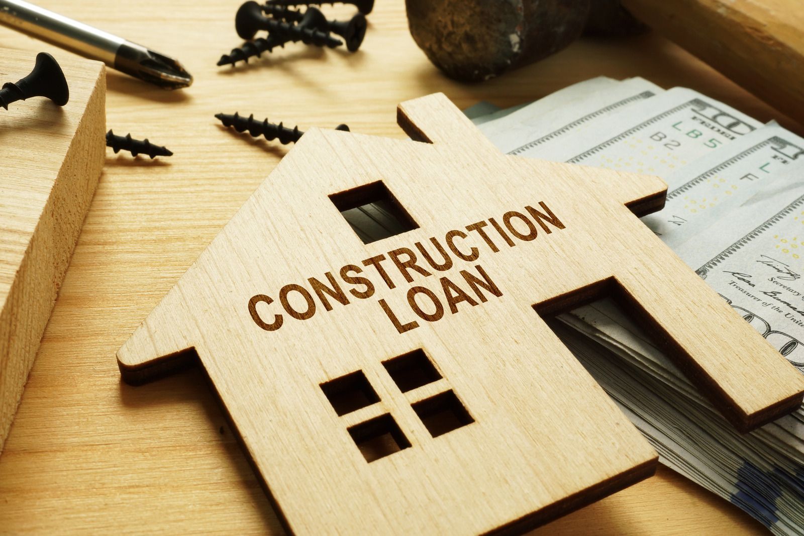 Wooden house model labeled “CONSTRUCTION LOAN” on desk with papers and a pen