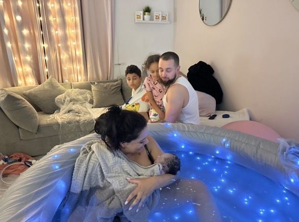 A woman is giving birth in an inflatable pool of water while a man and two children watch.