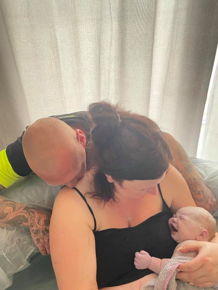 A man and woman are holding a baby in their arms after birthing in a pool
