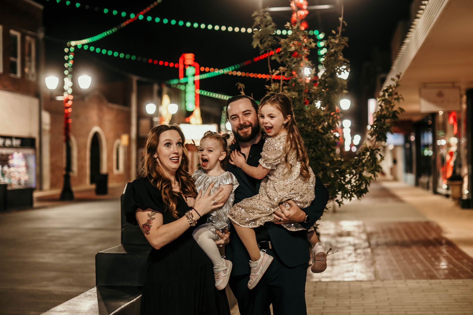 Family of four poses on a festive street at night with Christmas lights.