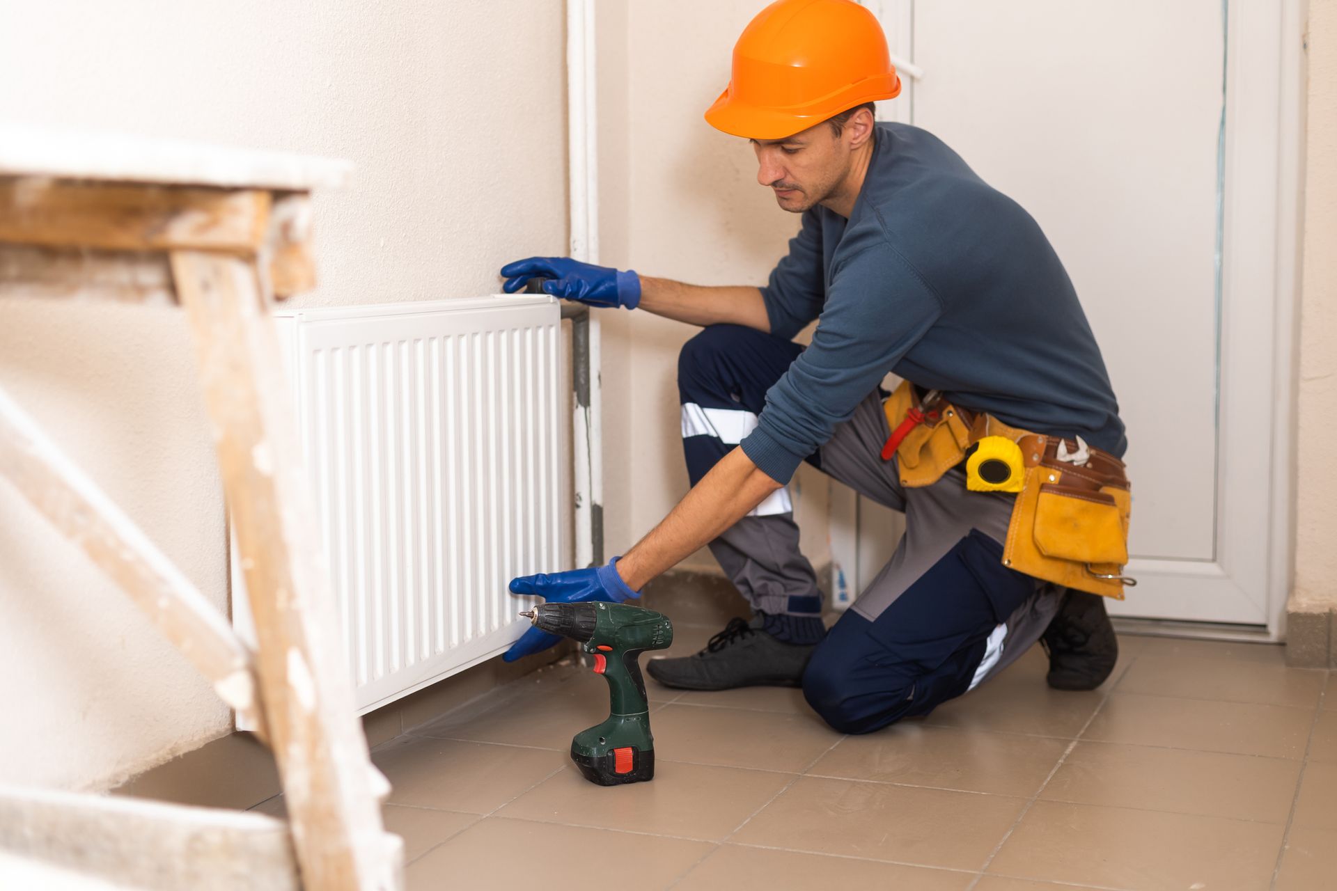 A heating contractor wearing an orange helmet and a blue uniform, performing heat pump services.